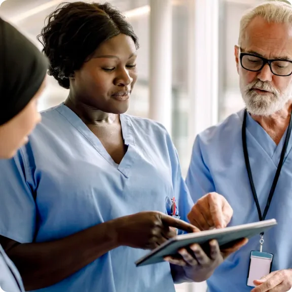 Drei medizinische Fachkräfte schauen sich ein Tablet an und diskutieren darüber.
