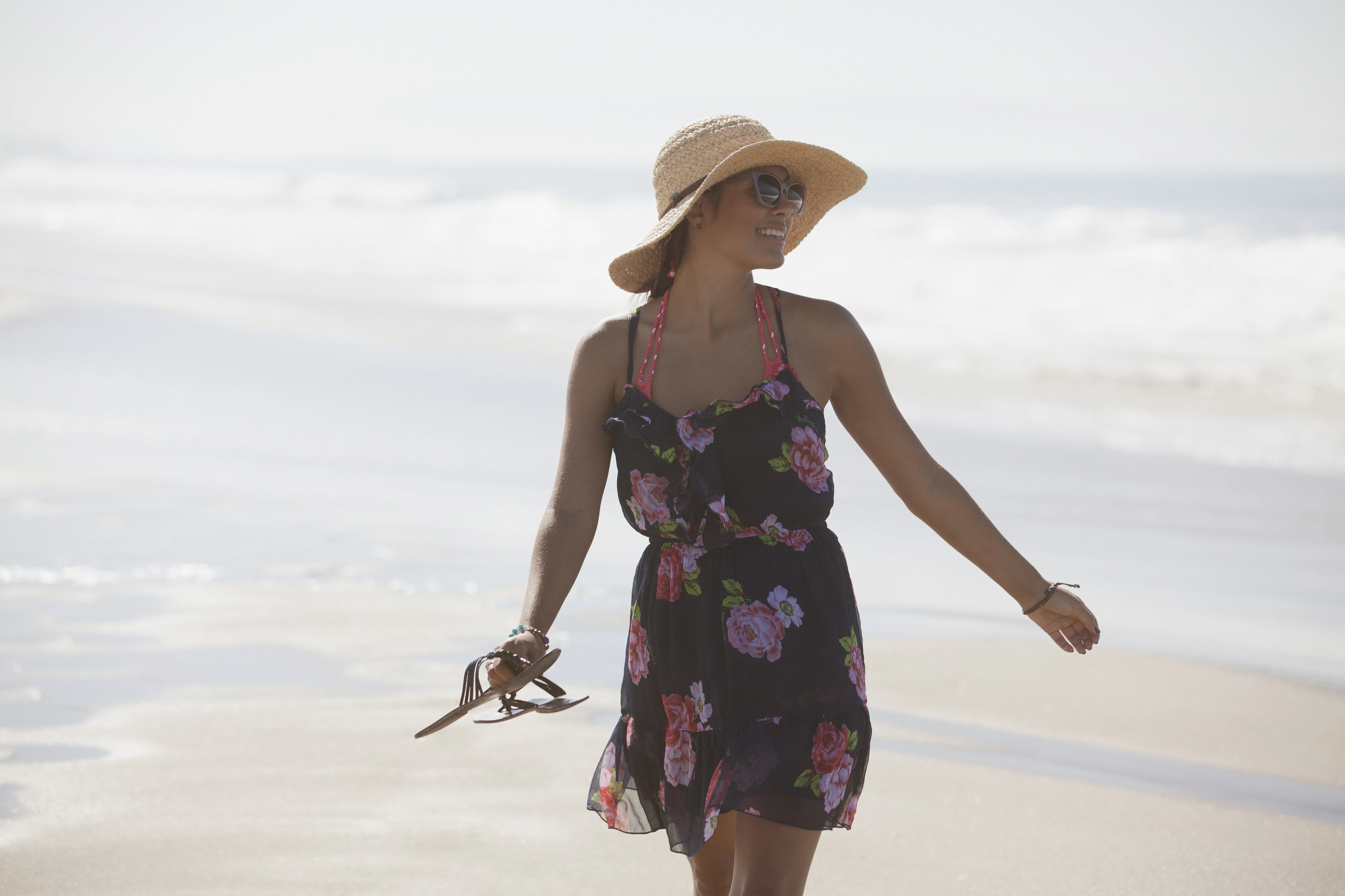Una mujer con vestido y sombrero caminando por una playa
