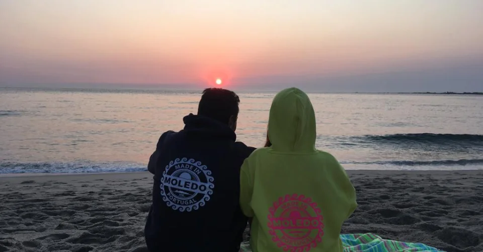 Sahilde oturmuş gün batımına bakan iki kişi